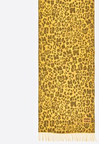 Bufanda amarilla con diseño de estampado de leopardo y detalles en marrón. Terminada con bordes con flecos. Etiqueta de la marca en la esquina inferior.