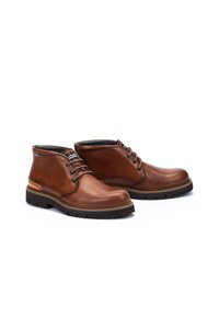 Bottes de cheville en cuir marron avec un bout rond, un laçage à l'avant et une semelle en caoutchouc texturée. Comprend des accents de couture et un panneau latéral contrastant.