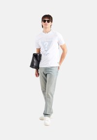 Camiseta de algodón blanca con un triángulo gráfico azul, jeans azul claro, bolso de mano negro y zapatillas blancas. Gafas de sol negras y collar de cadena.