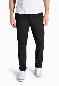 Schwarze, schmal zulaufende Hosen aus Baumwollmischgewebe, mit flachem Vorderteil, zwei seitlichen Taschen und umgeschlagenen Säumen. Kombiniert mit weißen Sneakers.
