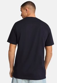 Donkerblauwe katoenen t-shirt, korte mouwen, ronde hals, eenvoudige design met zichtbare stiksels op de zoom en de mouwen. Achteraanzicht weergegeven.