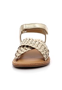 Sandalia de color beige tejido con una correa metálica dorada. Suela plana, diseño de punta abierta y correa ajustable en el tobillo. Acabado en cuero natural.
