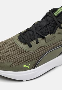 Des chaussures de sport en vert olive et mesh noir, avec des lacets noirs, une semelle en caoutchouc et un accent de logo vert vif sur le côté.
