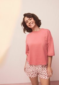 Lyserød bomulds T-shirt med korte ærmer, kombineret med hvide shorts med rødt hjerteprint. Simpelt design, afslappet pasform.