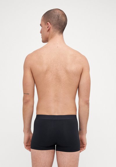 Boxer-briefs noirs avec une texture lisse et une taille élastique, portés par un modèle masculin de dos, sur fond neutre.