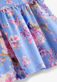 Jupe en tissu bleu clair avec un imprimé floral de fleurs roses et violettes et des colibris, design froncé avec une texture douce.