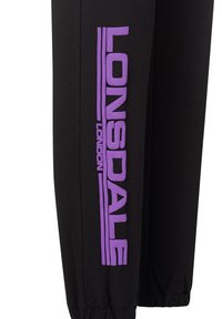 Black jogger pants featuring a large purple "LONSDALE" logo along the side, made of soft cotton material, with elasticated cuffs.