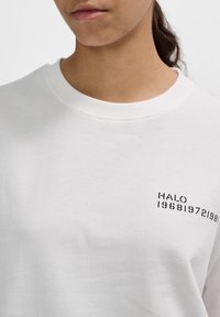 Biała bawełniana koszulka z okrągłym dekoltem i krótkimi rękawami, z czarnym nadrukiem na piersi, który głosi "HALO 196819721980".