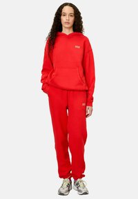 Sarkans džemperis un atbilstošas bikses, kokvilnas materiāls, pārāk liels izmērs, kangaroo kabata, neliela logotipa detaļa, strukturēta virsma, kopā ar tenisiem.