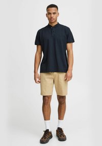 Navy polo shirt with short sleeves, button placket, paired with beige shorts. Brown and black sneakers with textured accents, white socks.