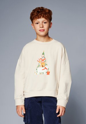 Cremefarbener Pullover mit einem bunten Baum-Graphic, das Tiere und Blätter zeigt. Lange Ärmel, gerippte Bündchen und eine lockere Passform. Kombiniert mit dunkelblauen Cordhosen.