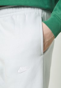 Light gray sweatpants made of soft fabric, featuring an elastic waistband and side pocket. A white Nike logo is embroidered on the upper thigh.