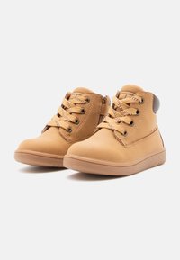 Bottines en cuir tan avec bouts ronds, cols rembourrés et lacets à l'avant. Semelles en caoutchouc texturé avec un détail contrastant au talon.