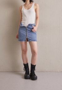 Denim minikjol med dragkedja framtill, ljusblå färg, hög midja och fransat fåll. Matchad med svarta kängor med snörning.