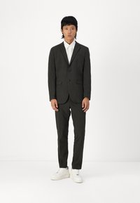 Costum gri închis cu carouri, ajustat pe corp, sacou cu un singur rând de nasturi și pantaloni asortați, purtate cu teniși albi.