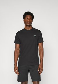 Zwart katoenen t-shirt met een ronde hals, korte mouwen en een klein groen Lacoste-logo op de borst, gecombineerd met zwarte shorts.