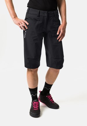 Zwarte shorts van lichtgewicht materiaal, met een knoopsluiting, twee voorkezen en een subtiel logo. Gecombineerd met zwarte schoenen en roze veters.