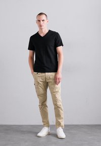 Zwarte korte mouwen v-hals t-shirt gecombineerd met beige cargobroek met zijzakken, aangevuld met witte sneakers.