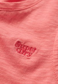 Camiseta de algodón color coral con un logotipo "Superdry" bordado en la parte delantera, en un color de hilo a juego. Tejido suave con un corte casual.