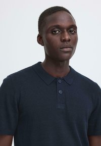 Polo bleu marine avec col, manches courtes et trois boutons. Confectionné dans un tissu texturé, présentant un motif tricoté subtil.