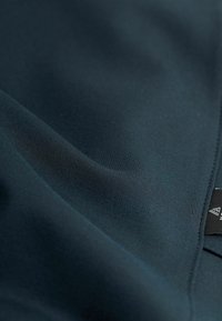 Jūras zilas audums ar gludu tekstūru, kam ir smalks spīdums, un malā ir uzlīme ar logotipu. Materiāls ir mīksts un elastīgs.