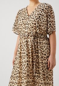 Abito leopardato con maniche corte, scollatura a v, vita con cintura e tessuto fluente. La palette di colori comprende beige, marrone e macchie nere.
