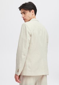 Ljusbeige linneblazer med en skräddarsydd passform, snedskurna slag, knappr detaljer på ärmarna och en mjuk textur. Bakvy visas.