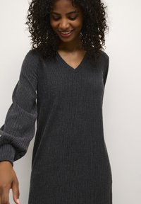 Robe tricotée grise à côtes avec un col en V et de longues manches bouffantes. Texture douce, coupe décontractée et design midi. Pas de motifs ni d'accents visibles.