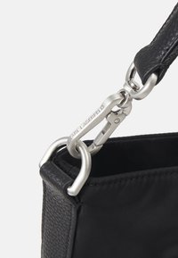 Czarna torba na ramię wykonana z teksturowanej skóry i gładkiego materiału. Zawiera srebrne metalowe okucia oraz wyraźne logo na zapięciu.