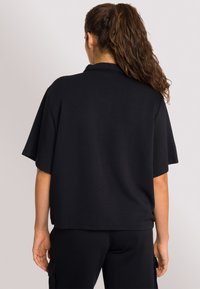T-shirt nera oversize con maniche corte, realizzata in tessuto morbido, caratterizzata da un design semplice e un orlo dritto, senza motivi o accenti visibili.
