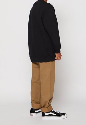 Schwarzer Sweatshirt mit lockerer Passform, beigefarbene Hose und schwarze Sneakers mit weißen Akzenten. Das Outfit betont lässigen Komfort und Einfachheit.