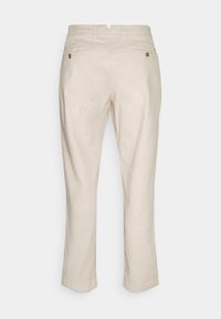 Beżowe lniane spodnie o prostym kroju nogawki, wyposażone w dwie tylne kieszenie i zdobione guzikami. Gładka faktura, długość 7/8.