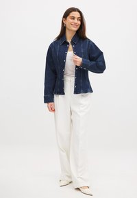 Denim button-up jacket in dark blue, featuring a collar, front snaps, and subtle stitching details, paired with cream wide-legged trousers.