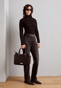 Haut à manches longues texturé noir, jeans taille haute noirs, large ceinture avec boucle dorée, sac à main noir avec accents dorés, et bottes noires pointues.