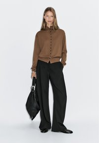 Maglione marrone con bottoni e colletto, abbinato a pantaloni neri a gamba larga e una borsa in pelle nera. Texture morbide evidenti.