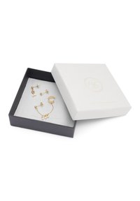 Conjunto de joyería de oro exhibido en una caja blanca texturizada con un interior gris. Incluye varias piezas con acentos de perlas y delicados detalles de cadena.
