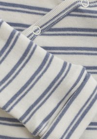 Randigt bomullstyg med blå och vita horisontella linjer, med en knapppdetails nära halsringningen och en mjuk, texturerad yta.