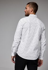 Bílá košile na knoflíky s černým abstraktním vzorem, s dlouhými rukávy, přizpůsobeným střihem a standardním límcem. Zobrazeno z zadní strany.