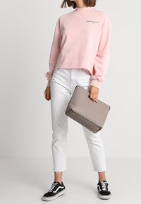 Vaaleanpunainen lyhyt collegepaita, jossa on teksti "cool girl", valkoiset nilkkapussihousut, mustat kangastennarit ja harmaa käsilaukku.