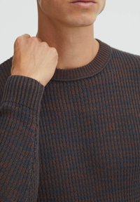 Knitted sweater featuring a ribbed texture in dark blue and brown, with a round neckline and fitted cuffs, focusing on fabric detail.