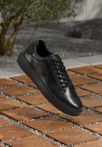 Zwarte leren sneakers met een ronde neus, vetersluiting aan de voorkant en een getextureerde rubberen zool. Aan de zijkant staat een subtiel reliëflogo.