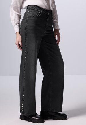 Zwarte spijkerbroek met wijde pijpen en hoge taille, versierd met zilveren studs langs de buitennaad. Gemaakt van denim met een gladde textuur. Past goed bij zwarte laarzen.