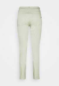 Jeans slim fit vert clair avec une texture lisse, dotés d'une taille, de deux poches arrière et de détails de couture subtils.