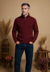 Bordeaux kabelgebreide trui met een hoge kraag en halve rits; gedragen met blauwe jeans. De achtergrond bevat natuurlijke elementen.