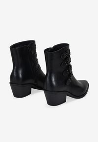 Bottines noires à finition lisse, avec trois sangles à boucles réglables sur le côté et un talon épais. Fermeture à glissière sur le côté.
