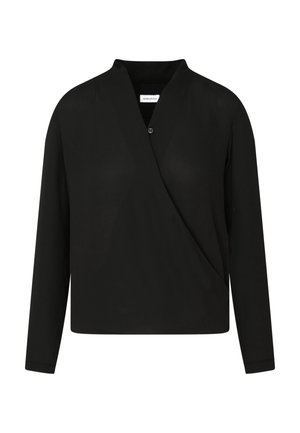 Vrouw draagt een zwarte wikkelblouse met lange mouwen, zwarte cropped rechte broek en zwarte sandalen met hoge hakken en enkelbandje.