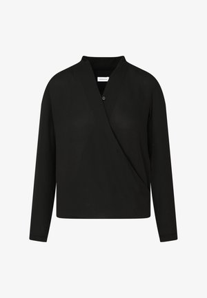 Vrouw draagt een zwarte wikkelblouse met lange mouwen, zwarte cropped rechte broek en zwarte sandalen met hoge hakken en enkelbandje.