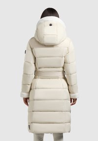 Beige puffer jack met een capuchon met een nepbont rand, een elastische riem en een verticale quiltdesign. Accenten zijn onder andere een logo patch bij de zoom.