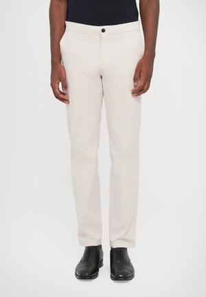 Pantaloni beige deschis dintr-un amestec de bumbac, cu croi drept, închidere frontală cu nasture, cu buzunare laterale și la spate, asortați cu pantofi negri.