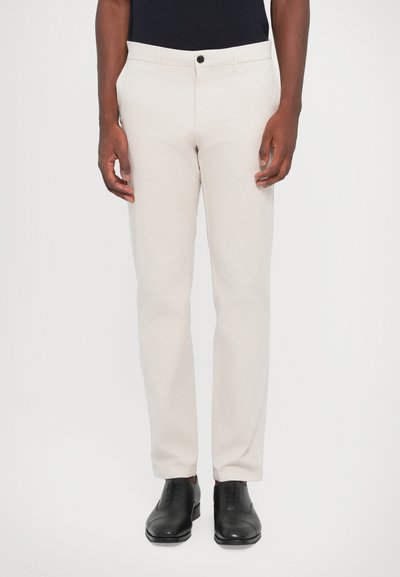 Pantaloni beige chiaro in misto cotone, design a gamba dritta, chiusura con bottone anteriore, con tasche laterali e posteriori, abbinati a scarpe nere.